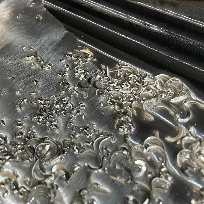 Ein Metallblock wird klein gefräst: Glänzende, gekräuselte Späne bedecken ihn, daneben gefräste Kanäle.