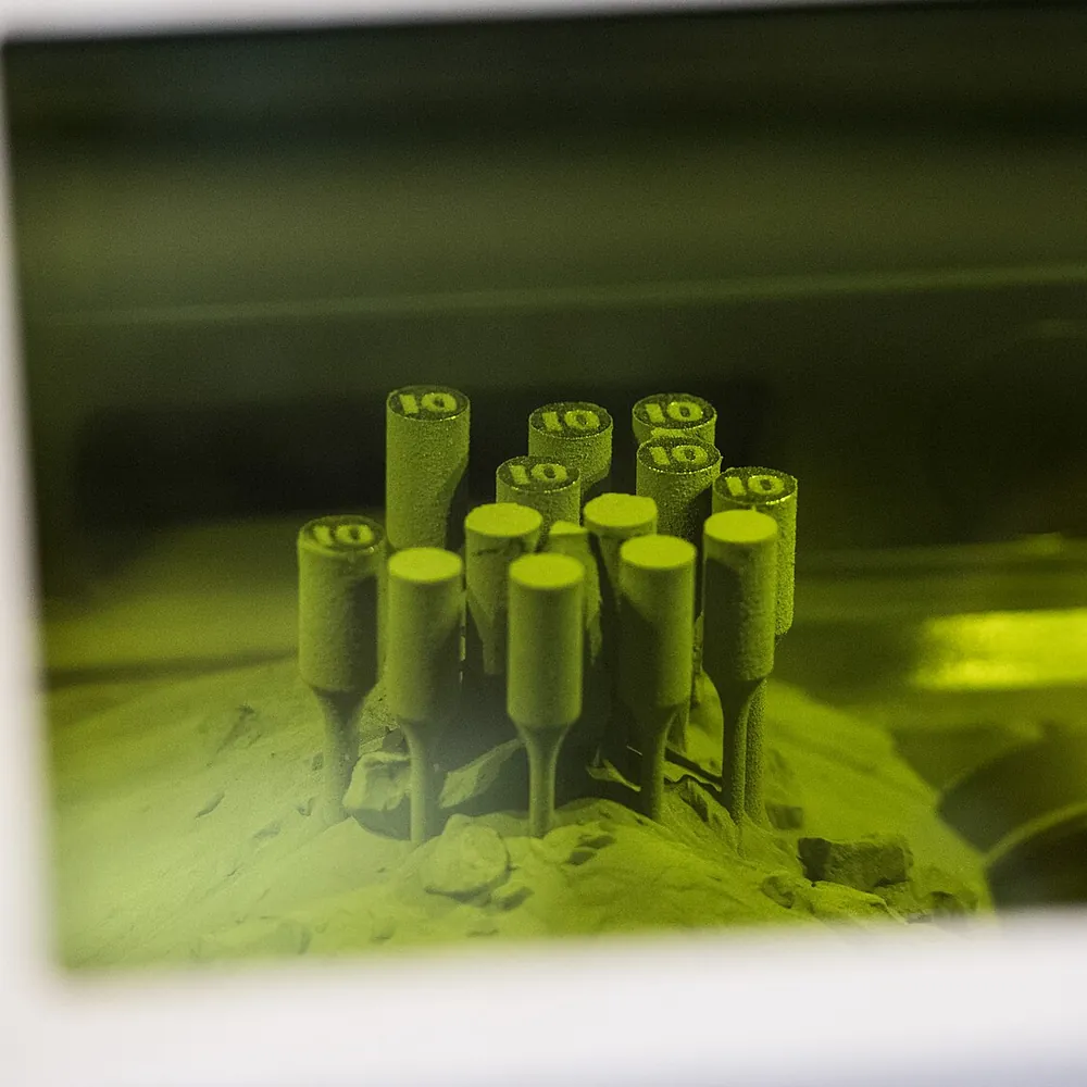 Durch das getönte Schutzfenster eines Laser-Pulverbettdruckers: Kleine Testteile stehen in dem Metallpulver, aus dem sie gedruckt wurden.