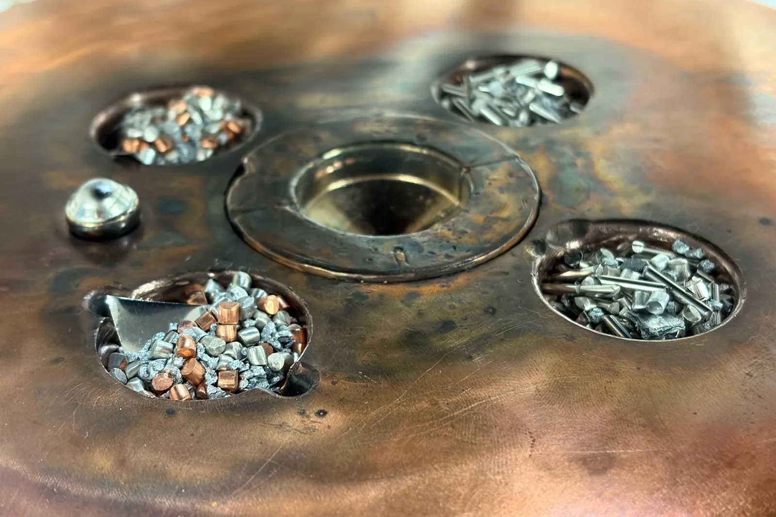 Close-up of a copper hearth: small pieces of raw metal loaded into its hollows, ready to be melted.