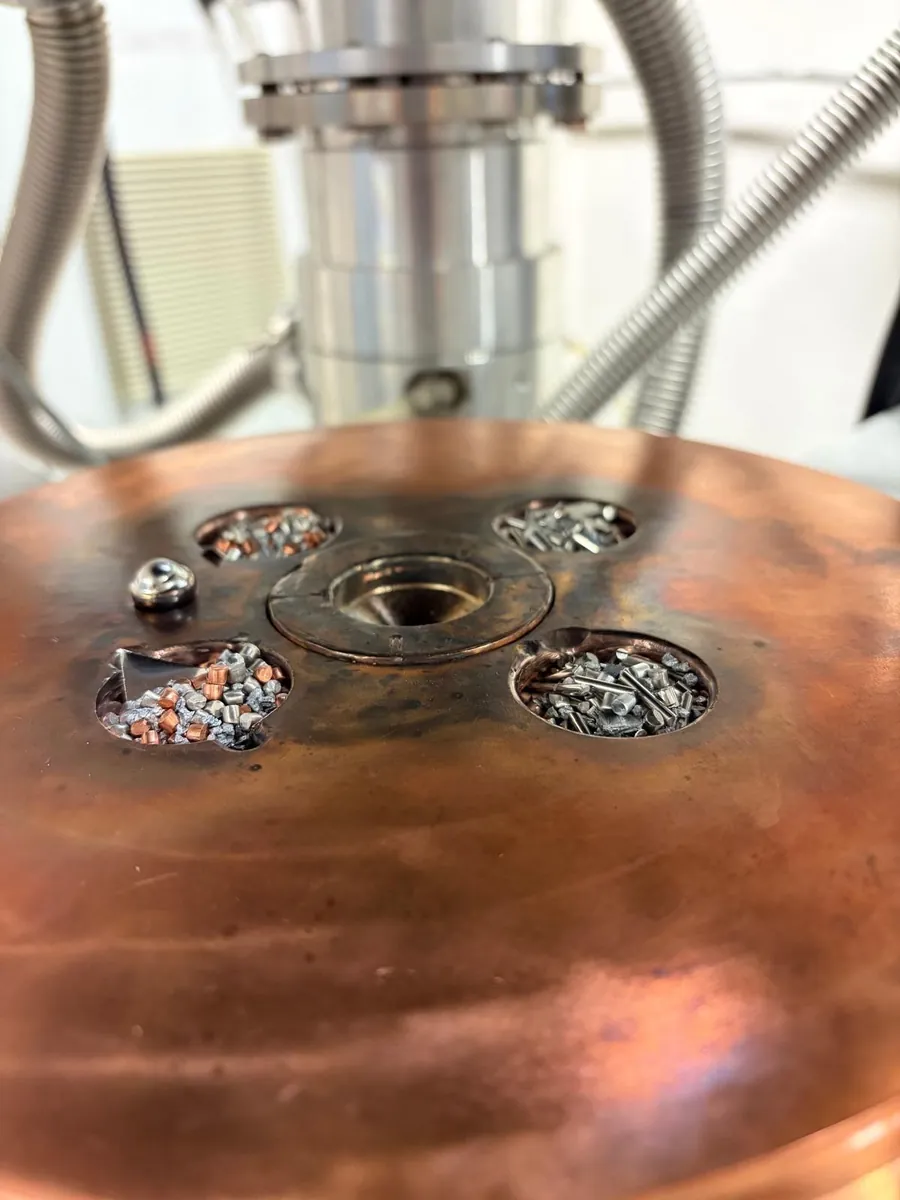 Close-up of the copper hearth: small pieces of raw metal in its hollows, ready to be melted.